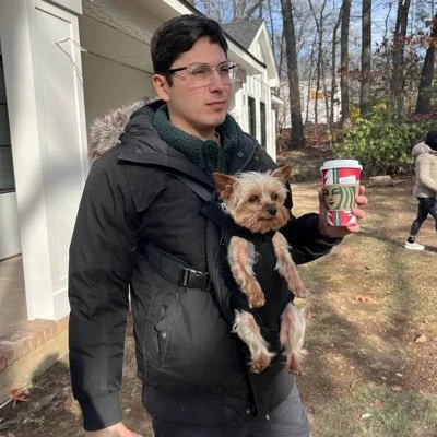 Viviano holding a Starbucks coffee with a dog in a front carrier